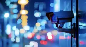 Alarm and Camera Registration - Security camera mounted on a building wall overlooking a city street at night with blurred lights in the background